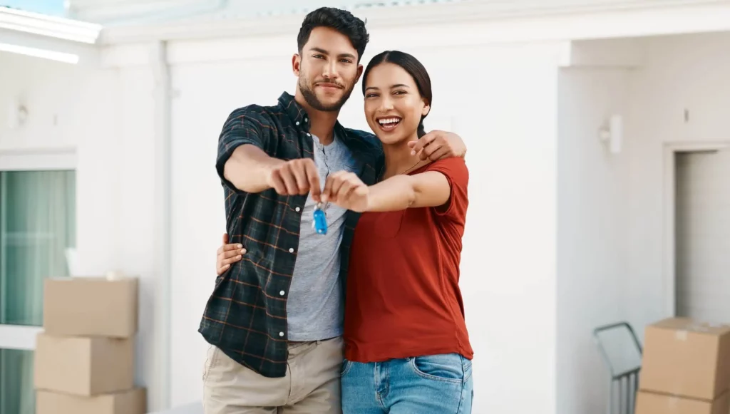 Imagem de um casal formado por um homem e uma mulher abraçados, sorrindo e segurando juntos a chave de uma casa para ilustrar matéria sobre como se cadastrar no Casa Paulista