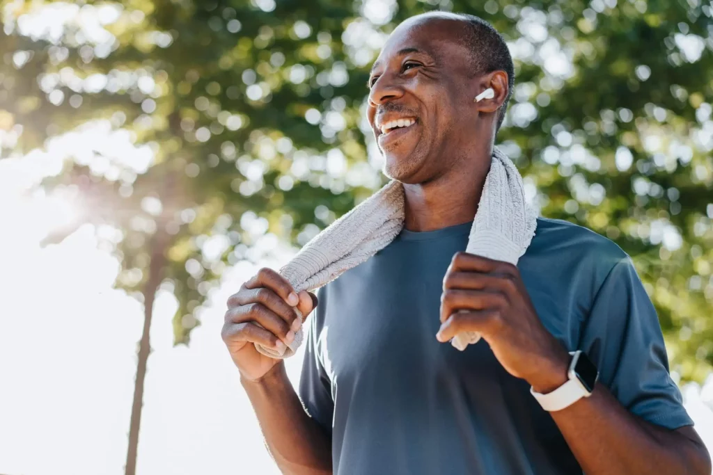 Imagem de um homem dando uma pausa no exercício físico do dia ao ar livre com uma tolha atrás do pescoço e um sorriso no rosto para ilustrar matéria sobre morar em cidade quente de São Paulo