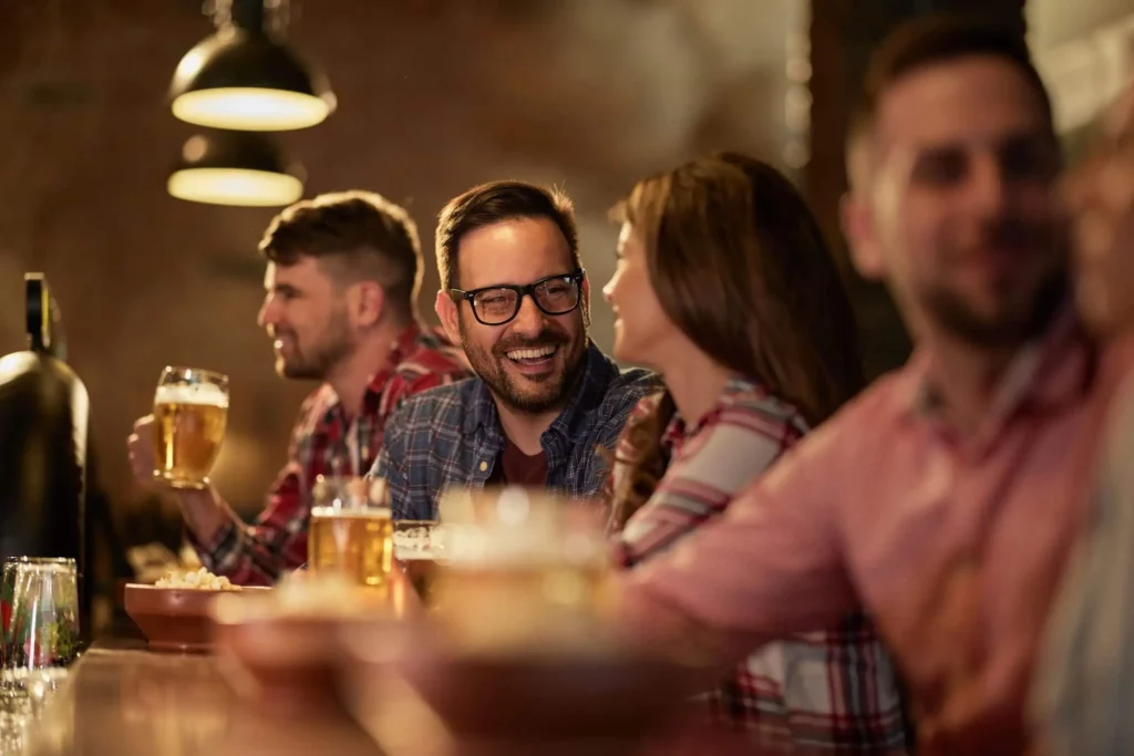  Imagem de um homem e uma mulher sentados no balcão de um pub conversando e sorrindo um para o outro para ilustrar matéria sobre o que fazer na Zona Norte de SP a noite