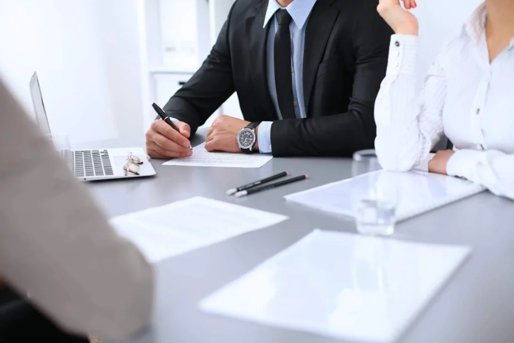 Imagem  de um grupo de três pessoas sentadas ao redor de uma mesa com papéis, canetas e computador em cima para ilustrar a matéria sobre passo a passo para transferir iptu de falecido