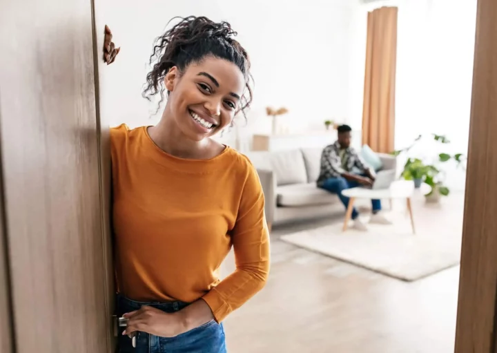 Imagem de uma mulher abrindo a porta de casa com um sorriso no rosto para ilustrar matéria sobre valor do condomínio