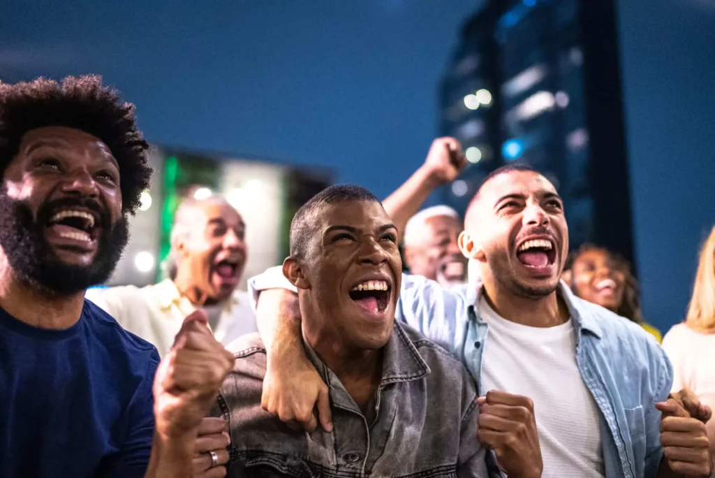 Imagem de alguns torcedores se abraçando, torcendo e sorrindo em sinal de comemoração para ilustrar matéria sobre o estádio mais bonito de São Paulo