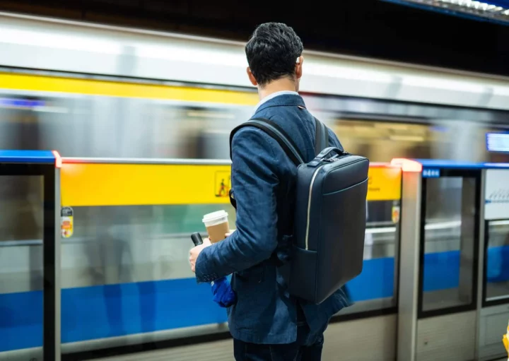 Imagem de um homem usando terno com uma mochila nas costas em uma estação de metrô esperando o trem para ilustrar matéria sobre a Linha Amarela do metrô de SP