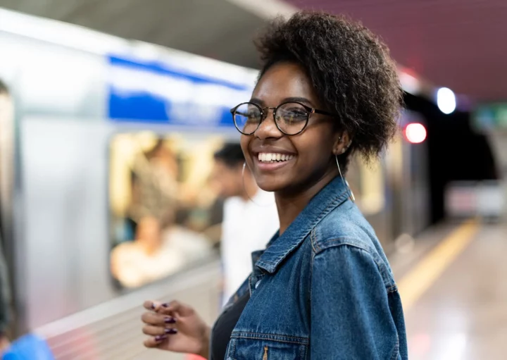 Imagem de uma mulher negra sorrindo em uma estação de metrô aguardando o trem abrir as portas para ilustrar matéria sobre a Linha 1-Azul do metrô de SP