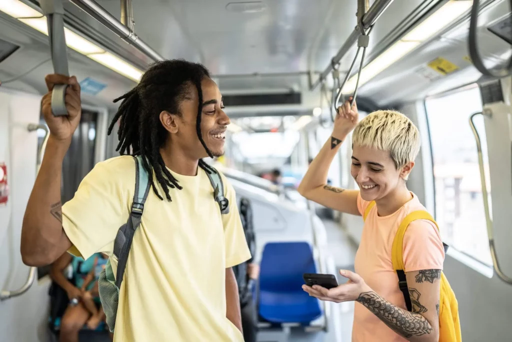 Imagem de duas pessoas em pé no metrô segurando nas barras de segurança sorrindo um para o outro para ilustrar matéria sobre as estações da linha verde do metrô de São Paulo