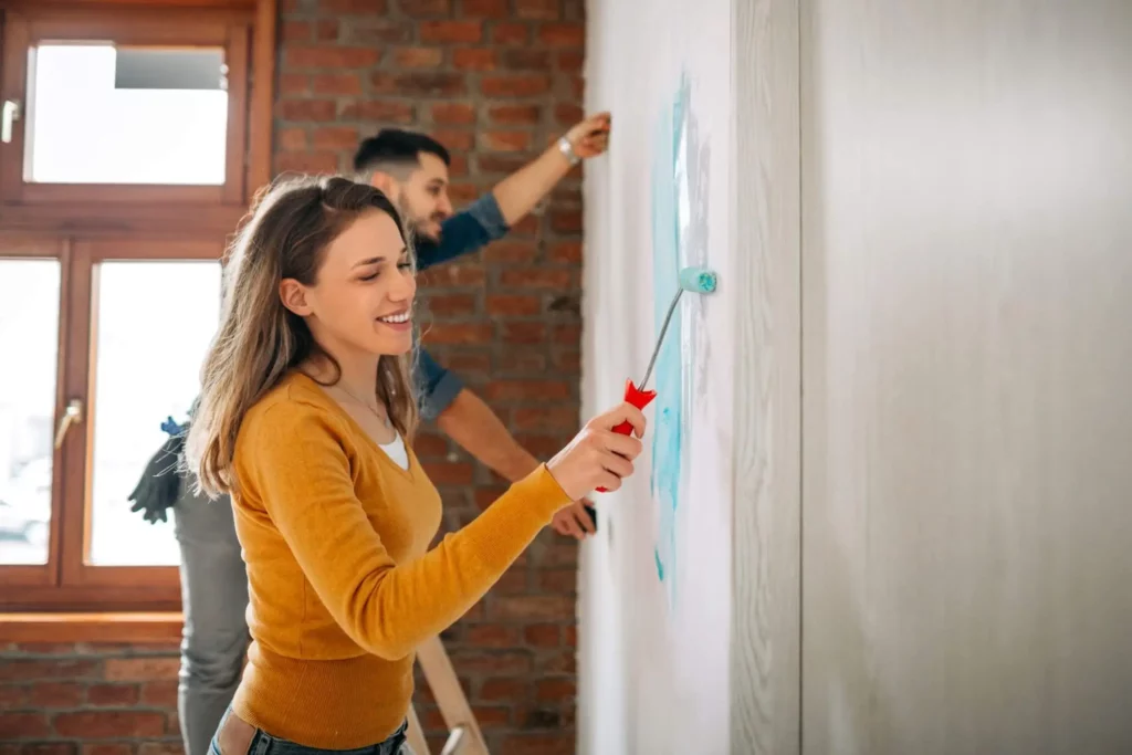 Imagem de um casal composto por um homem e uma mulher pintando a parede de um imóvel para ilustrar matéria sobre reformar ou construir