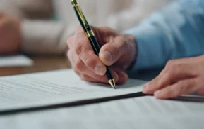 Foto de um homem assinando um documento.