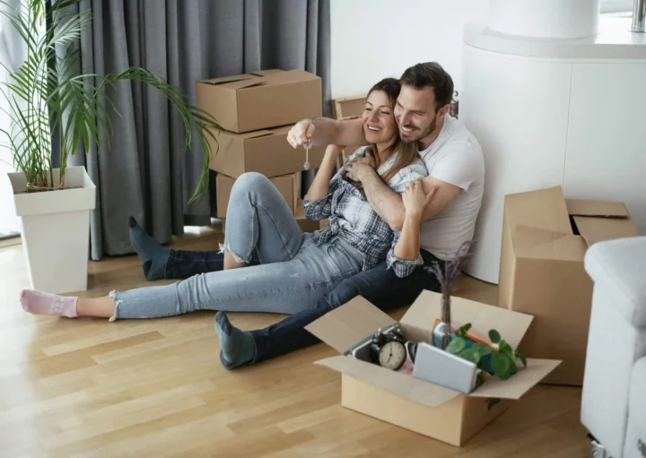 Imagem de um casal composto por um homem e uma mulher sentados no chão de uma casa ao lado de caixas de papelão para ilustrar matéria sobre o subsídio do Minha Casa, Minha Vida