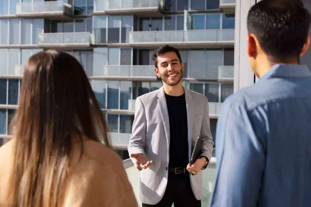 Imagem de um agente imobiliário conversando com um homem e uma mulher em frente a um prédio espelhado para ilustrar matéria sobre arrendamento de imóvel