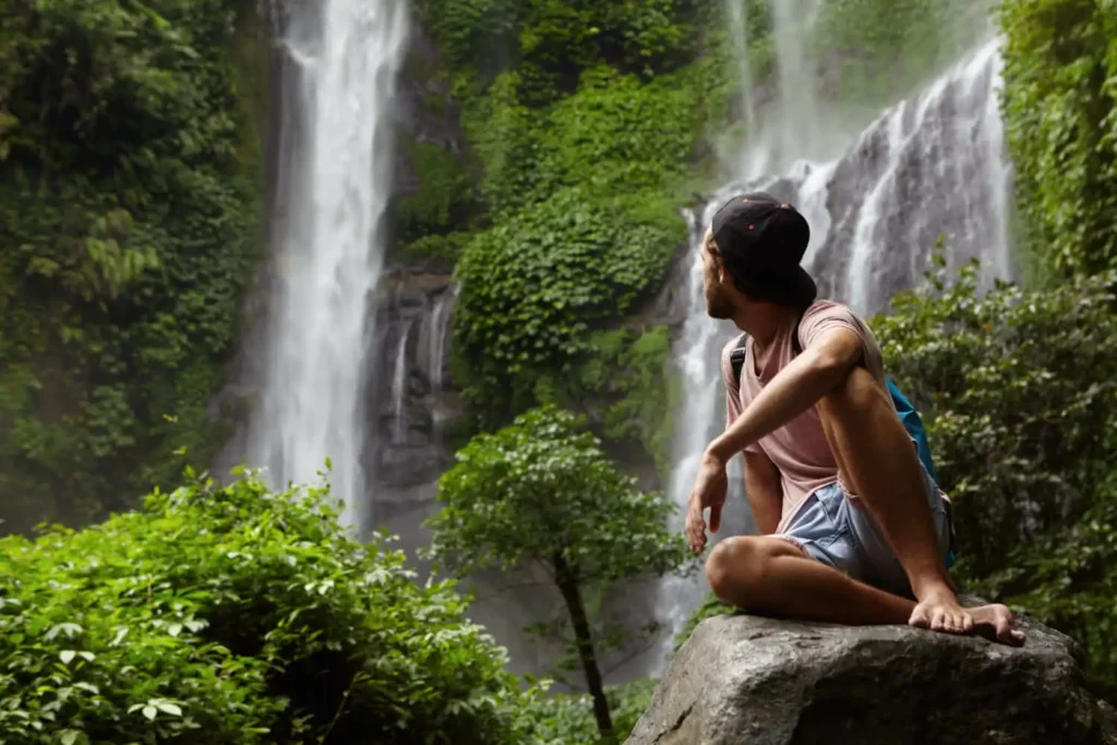 Imagem de homem sentado em uma pedra enquanto observa uma cachoeira para ilustrar matéria sobre cachoeira em São Paulo