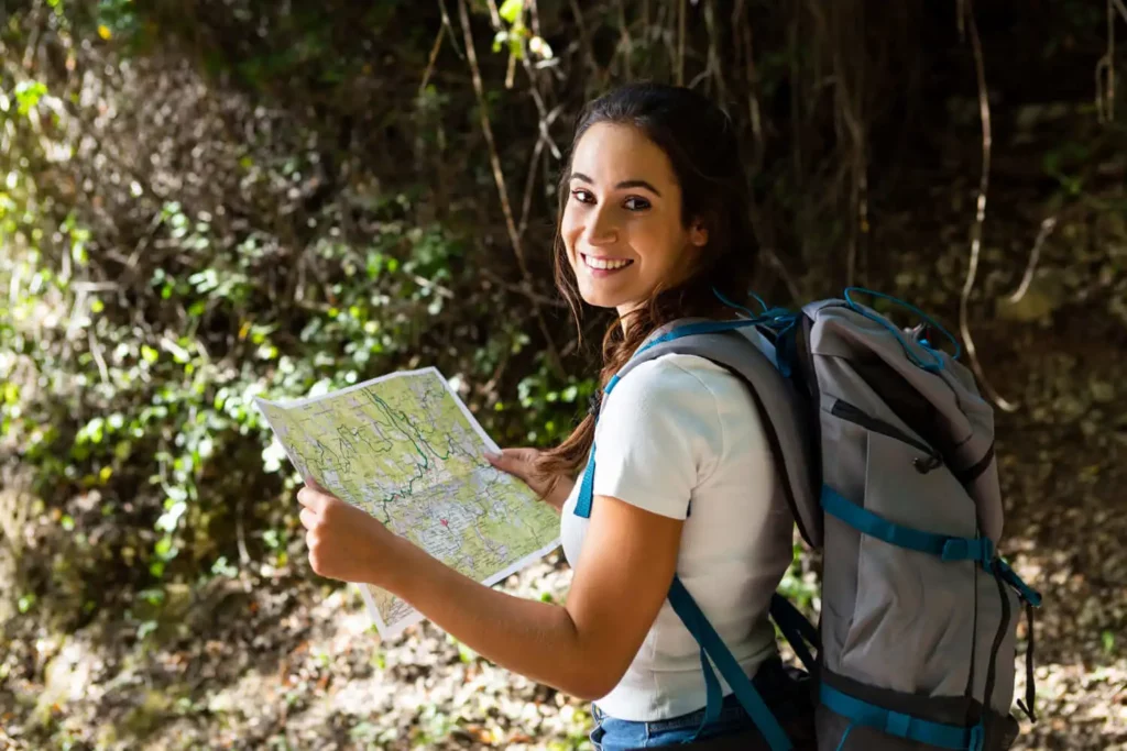 Imagem de  uma mulher sorrindo e segurando o mapa em uma trilha na mata para ilustrar matéria sobre as cachoeiras disponíveis na cidade de São Paulo