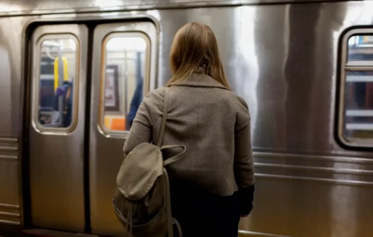 Imagem de uma mulher de costas com uma mochila pendurada nos ombros em frente a um trem em uma estação de metro para ilustrar matéria sobre a Linha 15-Prata