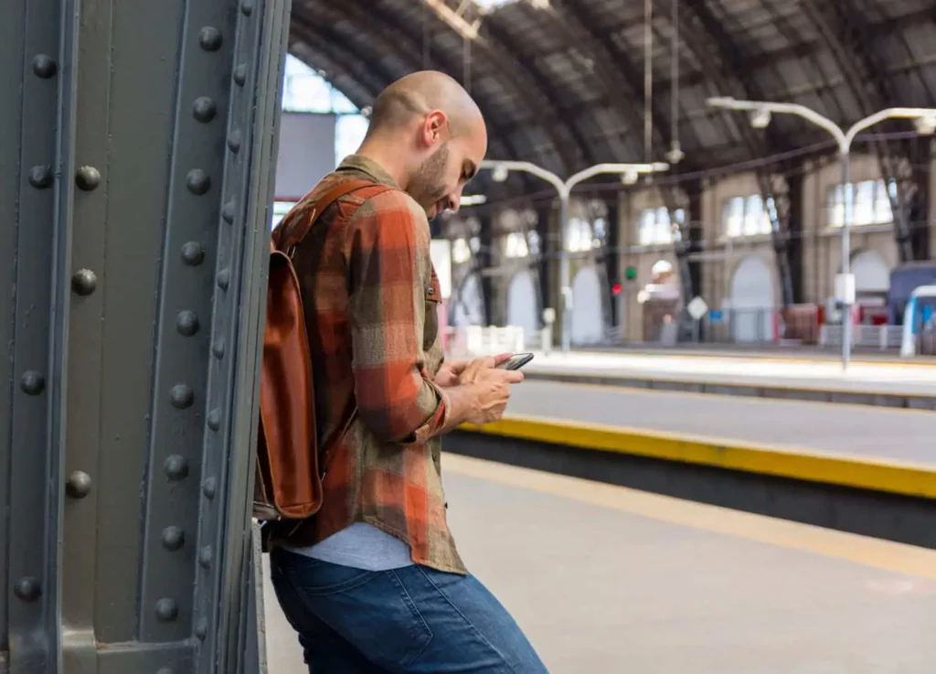 Imagem de um homem em uma estação de metrô encostado em uma pilastra enquanto olha para o celular para ilustrar matéria sobre a Linha 5-Lilás