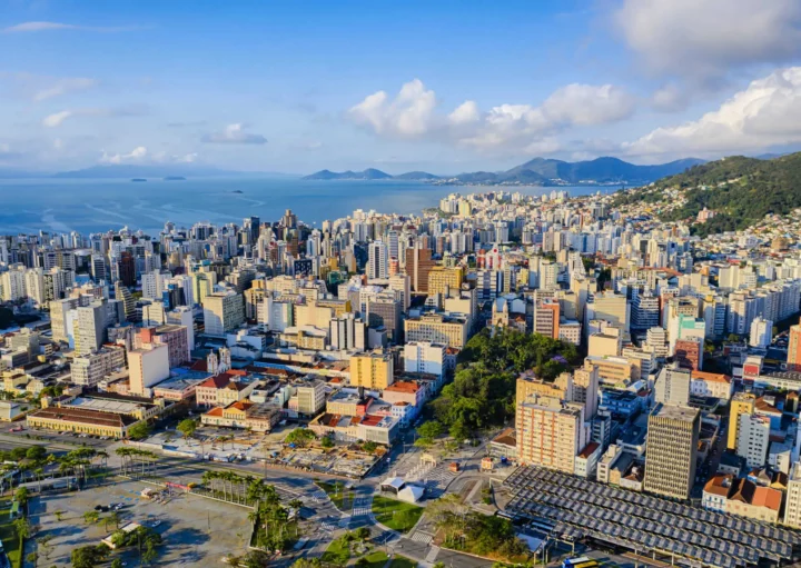 Imagem da vista aérea da capital de Santa Catarina mostra prédios, avenidas e mar ao fundo para ilustrar matéria sobre os bairros mais populosos de Florianópolis