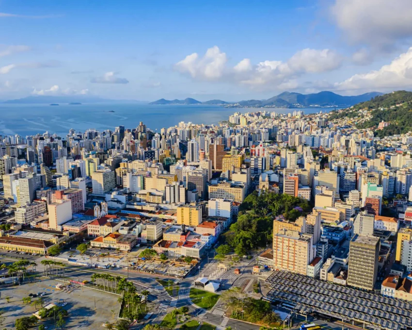 Imagem da vista aérea da capital de Santa Catarina mostra prédios, avenidas e mar ao fundo para ilustrar matéria sobre os bairros mais populosos de Florianópolis