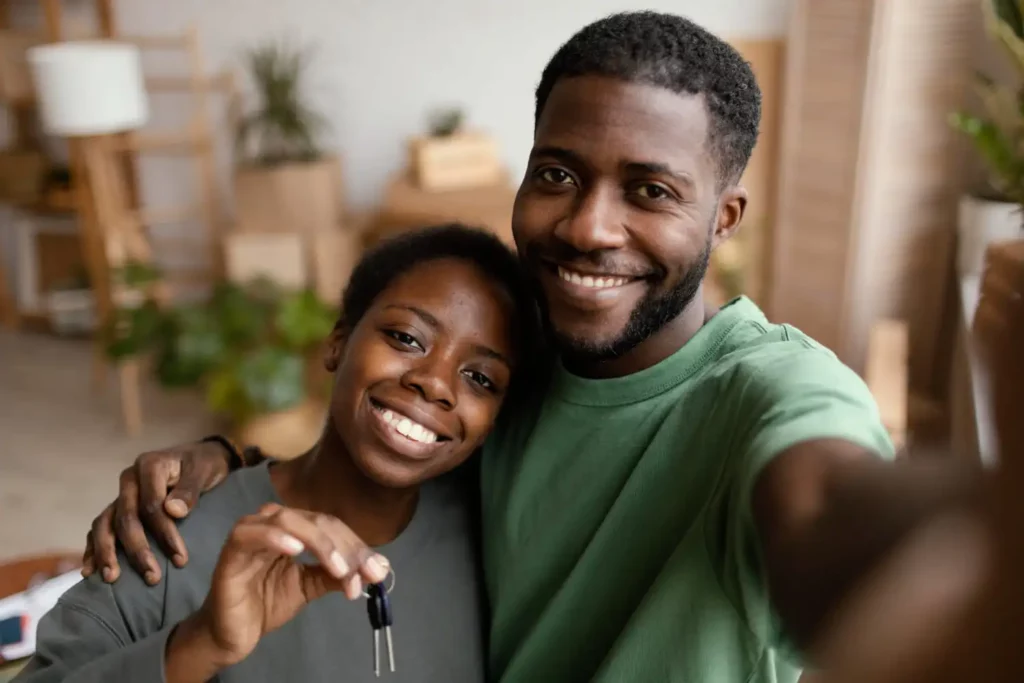 Imagem de um casal composto por um homem e uma mulher se abraçando de lado em uma casa enquanto seguram a chave de um imóvel para ilustrar matéria sobre se quem tem restrição pode financiar imóvel pela Caixa