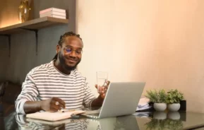 Foto que ilustra matéria sobre apartamento sem condomínio mostra um homem sentado com um laptop aberto a sua frente em uma mesa e um caderno ao lado (Foto: Shutterstock)