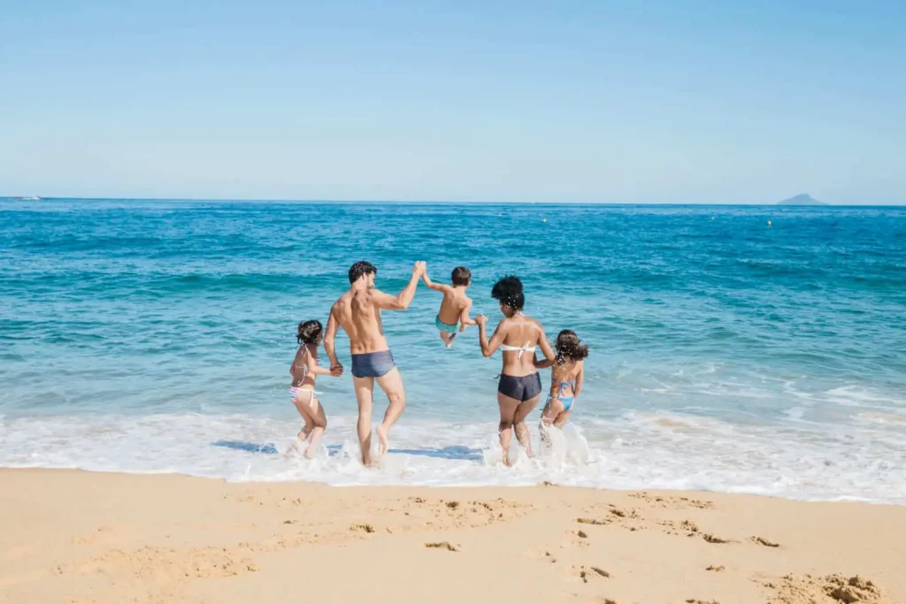 Imagem de uma família brincando enquanto anda em direção ao mar em um dia de sol e céu azul para ilustrar matéria sobre bairros bons e baratos para morar em Floripa