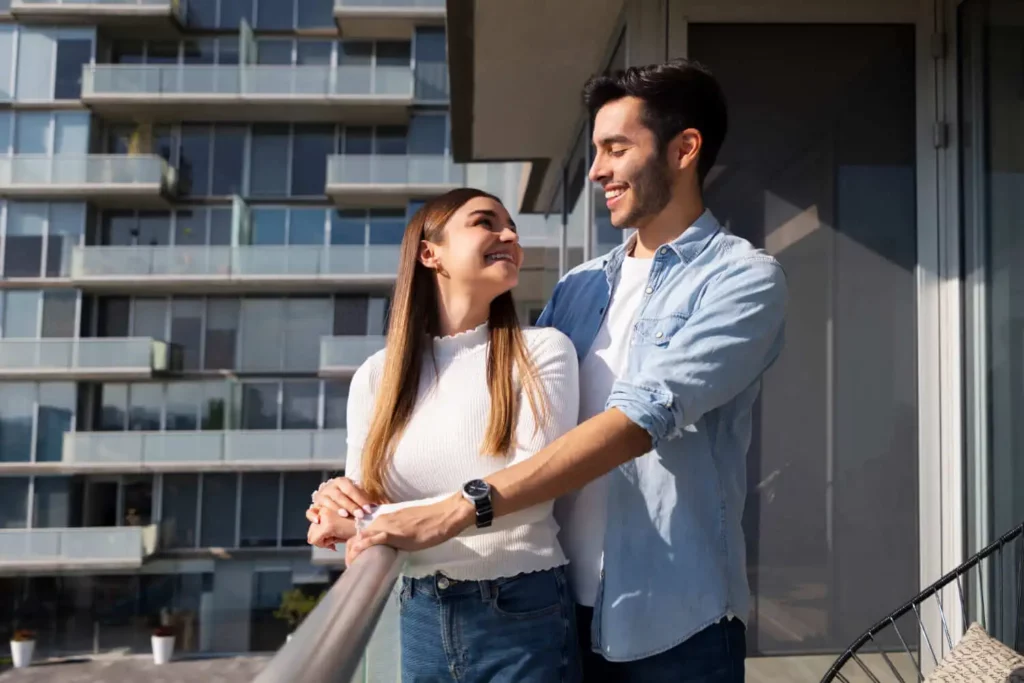 Imagem de um casal formado por um homem e uma mulher abraçados na sacada de um apartamento para ilustrar matéria sobre os riscos de vender um imóvel e aplicar o dinheiro