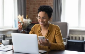 Foto que ilustra matéria sobre tecnologia no mercado imobiliário mostra uma mulher olhando a tela de um laptop enquanto segura um celular (Foto: Shutterstock)