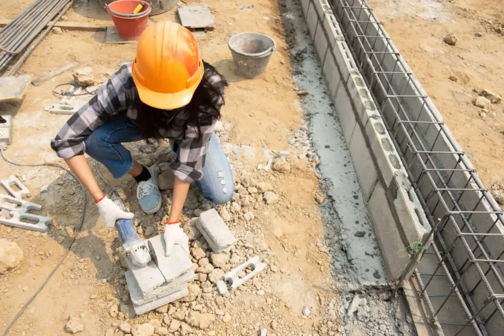 Imagem de uma mulher trabalhando em um canteiro de obra agachada enquanto mexe em tijolos de concreto para ilustrar matéria sobre valor do metro quadrado da construção